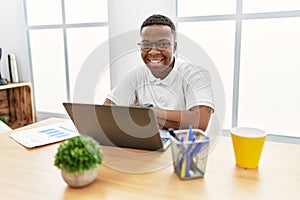 Young african man working at the office using computer laptop happy face smiling with crossed arms looking at the camera