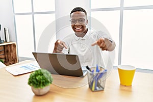 Young african man working at the office using computer laptop pointing to you and the camera with fingers, smiling positive and