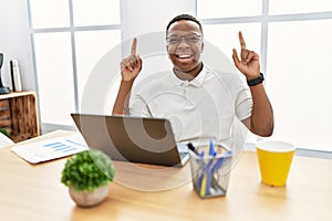 Young african man working at the office using computer laptop smiling amazed and surprised and pointing up with fingers and raised