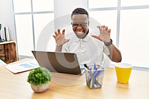 Young african man working at the office using computer laptop smiling funny doing claw gesture as cat, aggressive and sexy