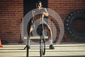 Young african man working out with battle ropes at a gym