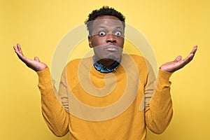 Young african man in yellow clothes shrugging shoulders