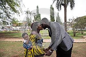 Young african mother with baby on her back kisses her husband. Family concept