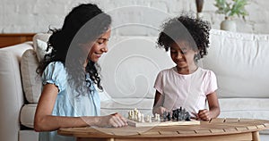 Young African mother and little daughter play chess at home