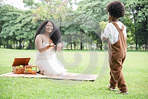 Young African mother smiling and getting little flowers tree from her son at garden. African family sitting on mat picnic together