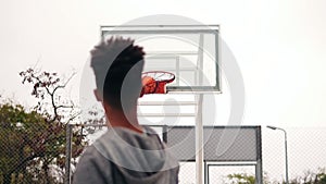 Young african player jumping up and throwing ball in a basketball hoop, the ball hits the ring and scores. The man turns