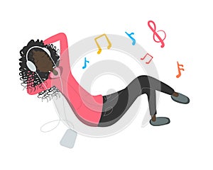 Young african pretty woman lies on the floor and listens music tunes by big headphones. Girl looks joyful relaxed and happy.