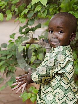 Young African school boy holding hands under a tap. Water scarcity problems concern the inadequate access to safe drinking water.