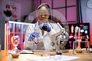 Young african scientist with test tube and microscope making research in clinical laboratory.