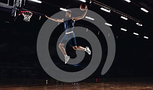 Young African sportsman, basketball player training in gym, idoors isolated on dark background. Concept of sport, game