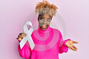 Young african woman with afro hair holding pink cancer ribbon celebrating achievement with happy smile and winner expression with