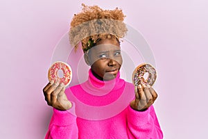 Young african woman with afro hair holding tasty colorful doughnuts skeptic and nervous, frowning upset because of problem