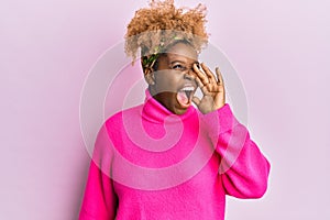 Young african woman with afro hair wearing casual winter sweater shouting and screaming loud to side with hand on mouth