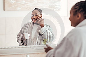 Young African woman applying face cream in the bathroom