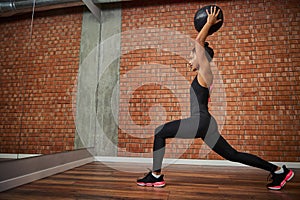 Young African woman, athlete with a beautiful muscular body doing exercises on the buttocks - lunges, holding a medical gymnastic