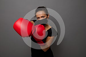 Young African woman boxer in black medical protective mask and red boxing gloves, punching towards camera, making direct hit,