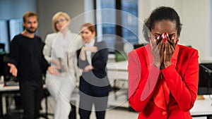 Young african woman crying because of the ridicule of colleagues. Racial discrimination in the office.