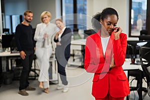 Young african woman crying because of the ridicule of colleagues. Racial discrimination in the office.