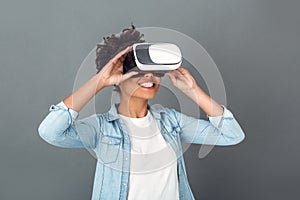 Young african woman isolated on grey wall studio casual daily lifestyle holding virtual reality headset