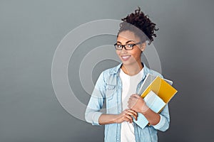 Young african woman isolated on grey wall studio casual daily lifestyle student holding notebooks smiling photo