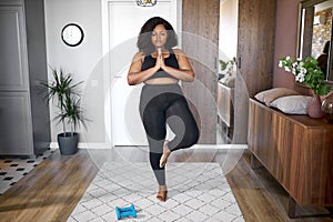 Young african woman keep balance, stand on one leg, yoga time at home