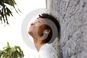 Young african woman leaning to a wall outside and looking up