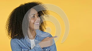 Young African Woman Pointing at Product, Yellow Background