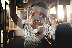 Young African woman riding on a bus listening to music