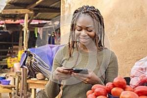 young african woman selling in a local african market using her mobile phone and credit card to do a transaction online smiling