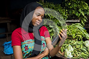 Young african woman selling in a local market feeling sad and dejected while looking at her phone