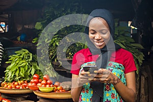 Young african woman selling in a local market smiling while using her mobile phone