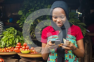Young african woman selling in a local market smiling while using her mobile phone