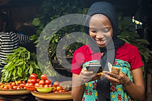 Young african woman selling in a local market smiling while using her mobile phone