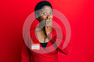 Young african woman with short hair wearing hello my name is sticker identification covering mouth with hand, shocked and afraid