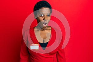 Young african woman with short hair wearing hello my name is sticker identification scared and amazed with open mouth for