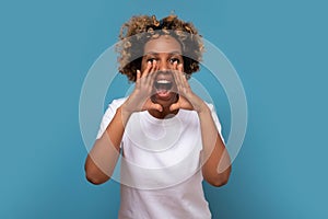 Young african woman shouting and screaming loud to camera with hand on mouth