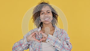 Young African Woman showing Heart Shape by Hands on Yellow Background