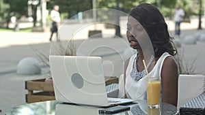 Young african woman sitting alone in a cafe having a videoconferance on a laptop