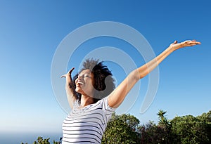 Young african woman standing outdoors with arms raised and laughing