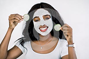 Young African woman in studio with refreshing cucumber facial mask on her face, for young and beautiful skin and