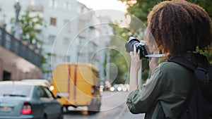 Young African woman tourist with curly hair and backpack travelling, photographing attractions using digital device