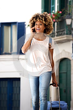 Young african woman traveling with bag and talking on smart phone outdoors