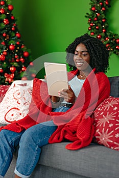 Young african woman using digital tablet and smiling while resting at home decorated for Christmas.