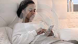 Young African Woman Using Smartphone while Relaxing in Bed