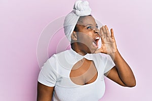 Young african woman wearing hair turban over pink background shouting and screaming loud to side with hand on mouth