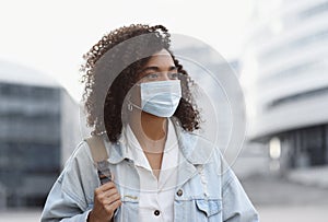 Young african woman wearing protective face mask in a city. Mixed race student girl on a city street.