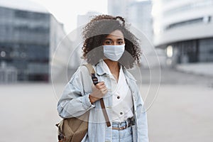 Young african woman wearing protective face mask in a city. Mixed race student girl on a city street.
