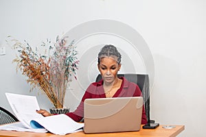 Young African woman is working at a table in a modern office setting.