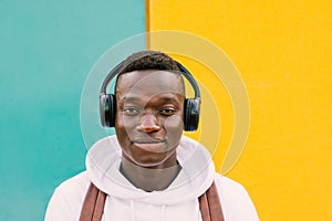 Young afro American black man listening music with wireless headphones while wearing a white sweatshirt and a backpack