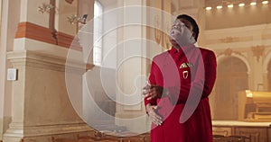 Young afro american emotional singer performing worship music. Male person wearing red suit moving hands while singing